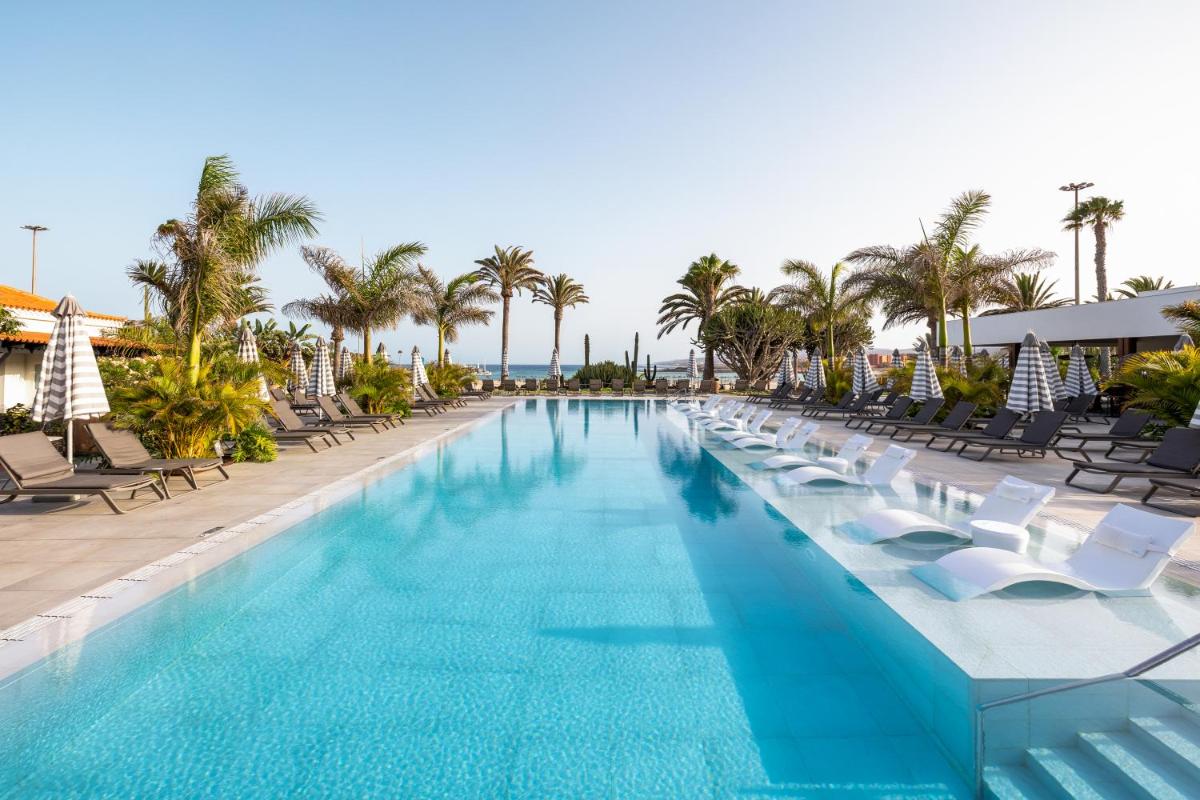 Una gran piscina con sillas y palmeras. en Barceló Fuerteventura Royal Level - Adults Only, en Caleta de Fuste
