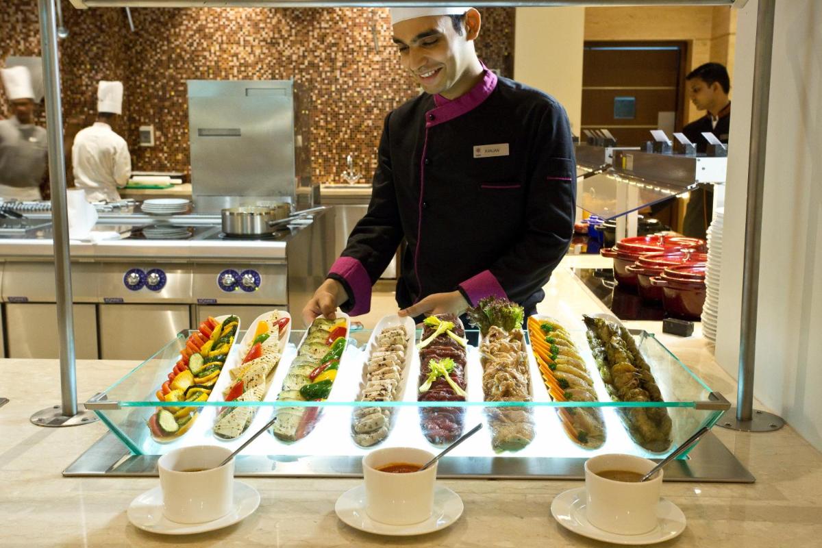 a man standing in a kitchen preparing food at The Suryaa New Delhi in New Delhi a man standing in a kitchen preparing food at The Suryaa New Delhi in New Delhi