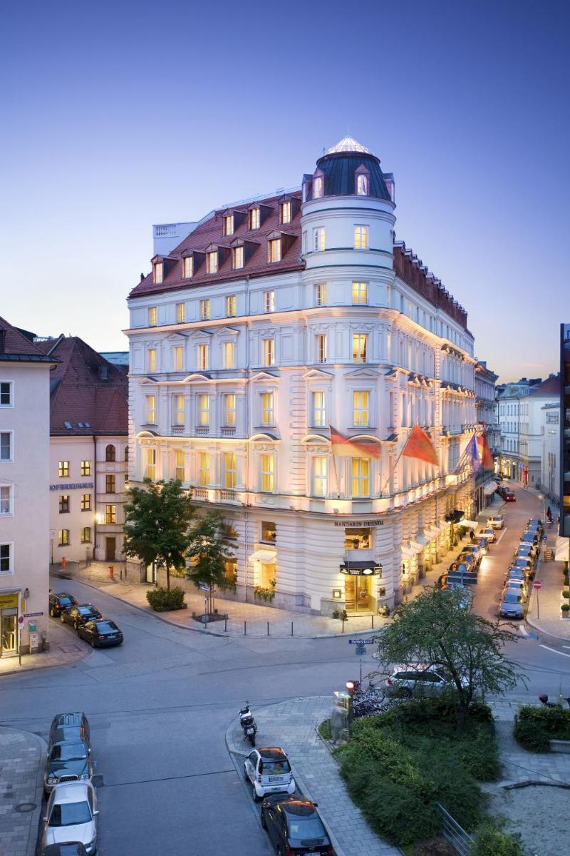 ein großes weißes Gebäude mit auf einem Parkplatz geparkten Autos in der Unterkunft Mandarin Oriental, Munich in München