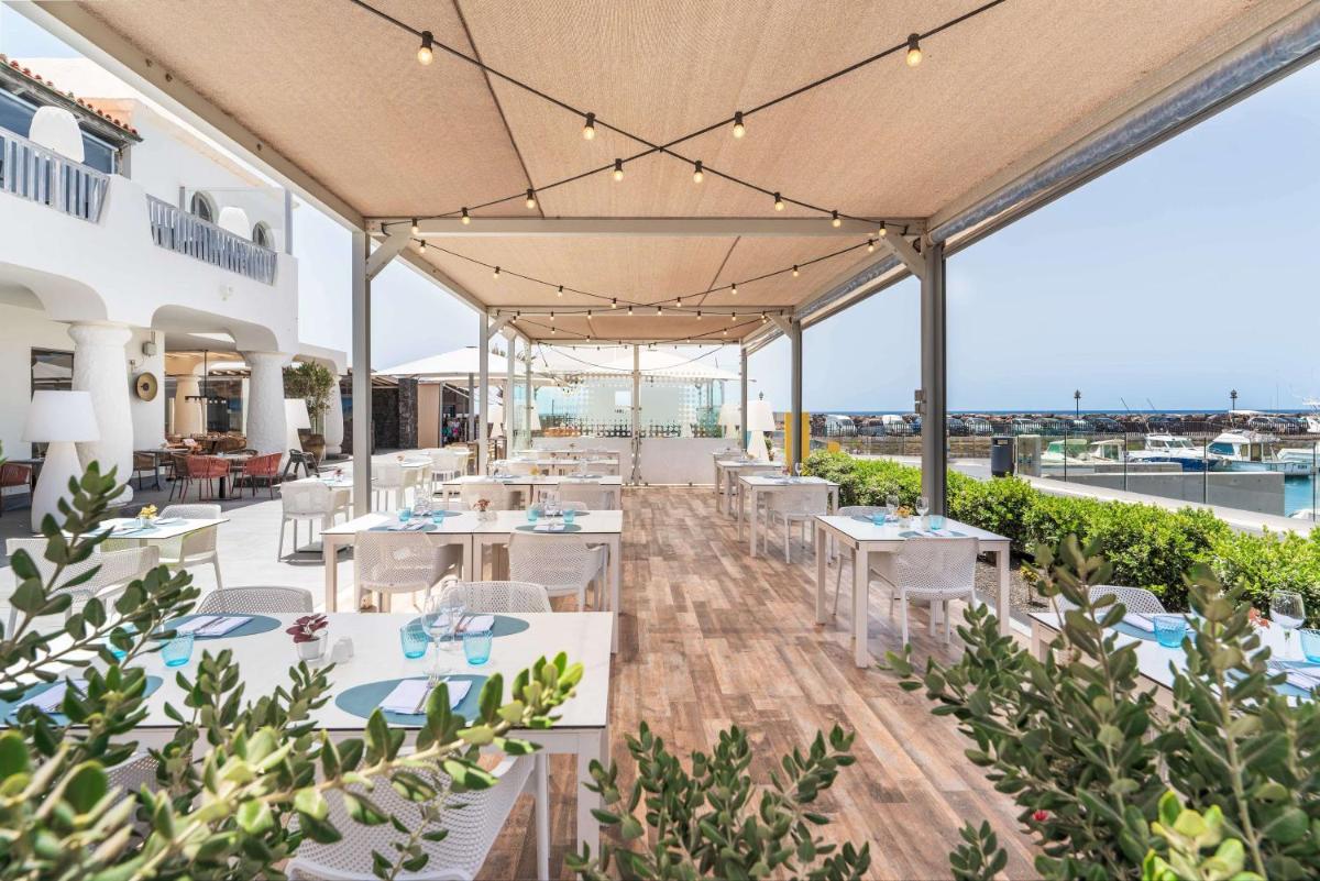 Un restaurante con mesas y sillas blancas y vista al mar. en Barceló Fuerteventura Castillo, en Caleta de Fuste