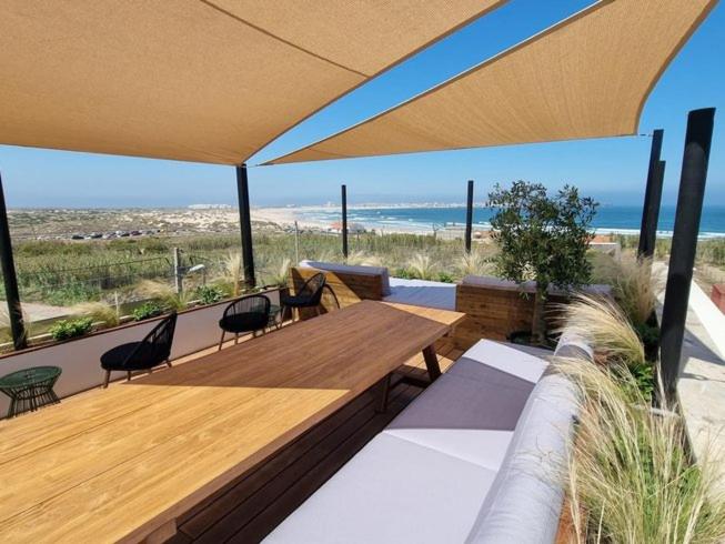 um pátio com uma mesa e cadeiras de madeira e a praia em The Salty Pelican Yoga & Surf Retreat em Peniche