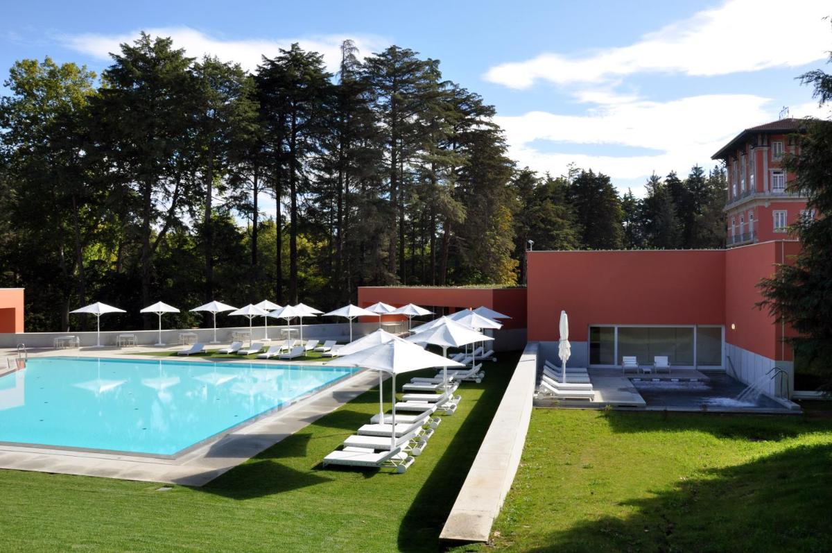 uma piscina com cadeiras e guarda-sóis ao lado de um prédio em Vidago Palace em Vidago