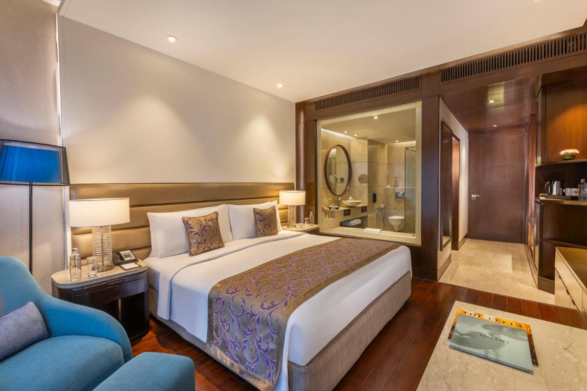 a bedroom with a large bed and a blue couch at The Leela Ambience Convention Hotel Delhi in New Delhi