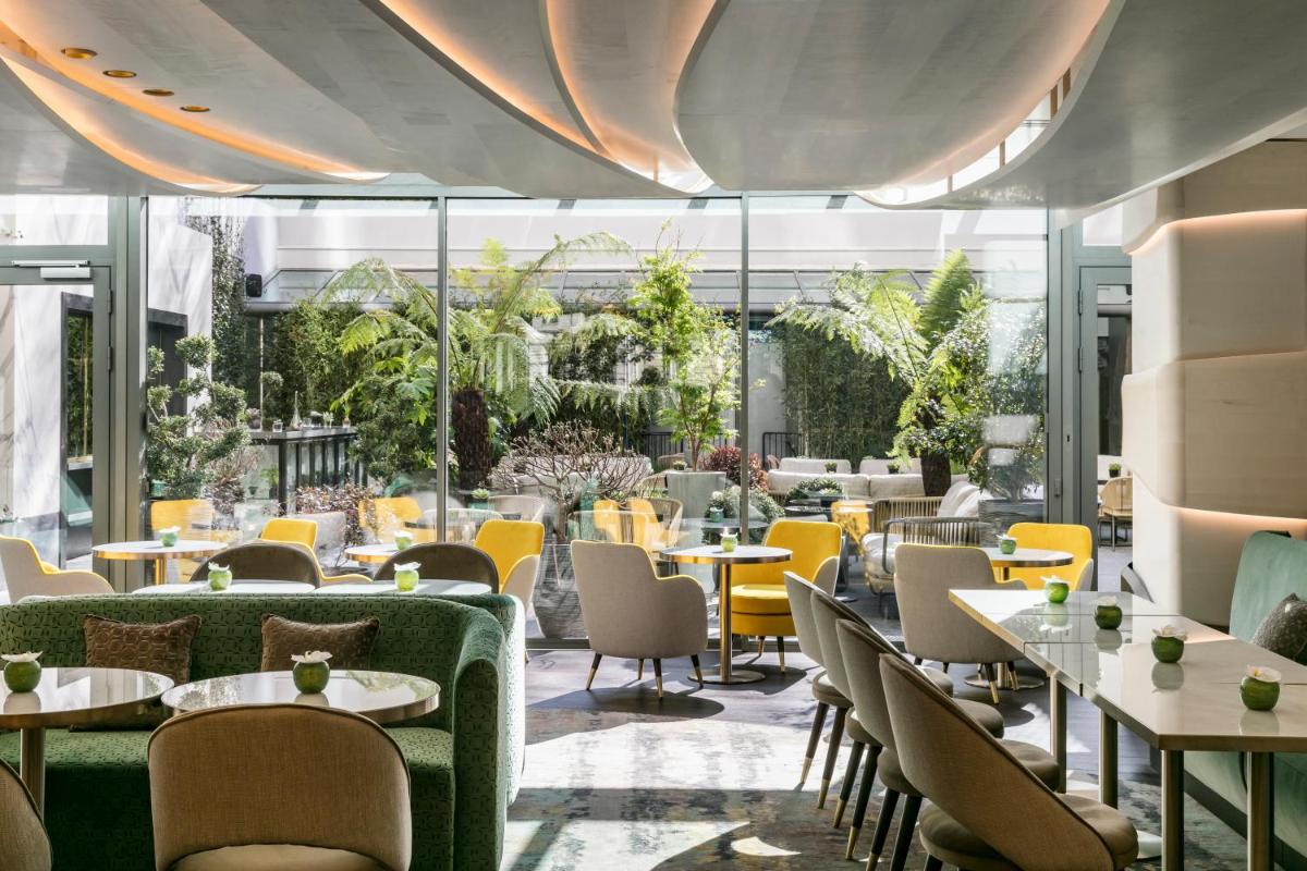 un restaurant avec des tables, des chaises et des fenêtres dans l'établissement L'Hôtel du Collectionneur Paris, à Paris