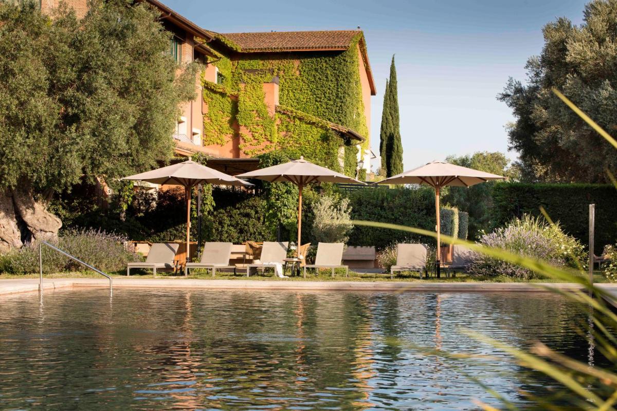 Una piscina con sombrillas y sillas al lado de un edificio. en Hotel Peralada Wine Spa & Golf, en Peralada