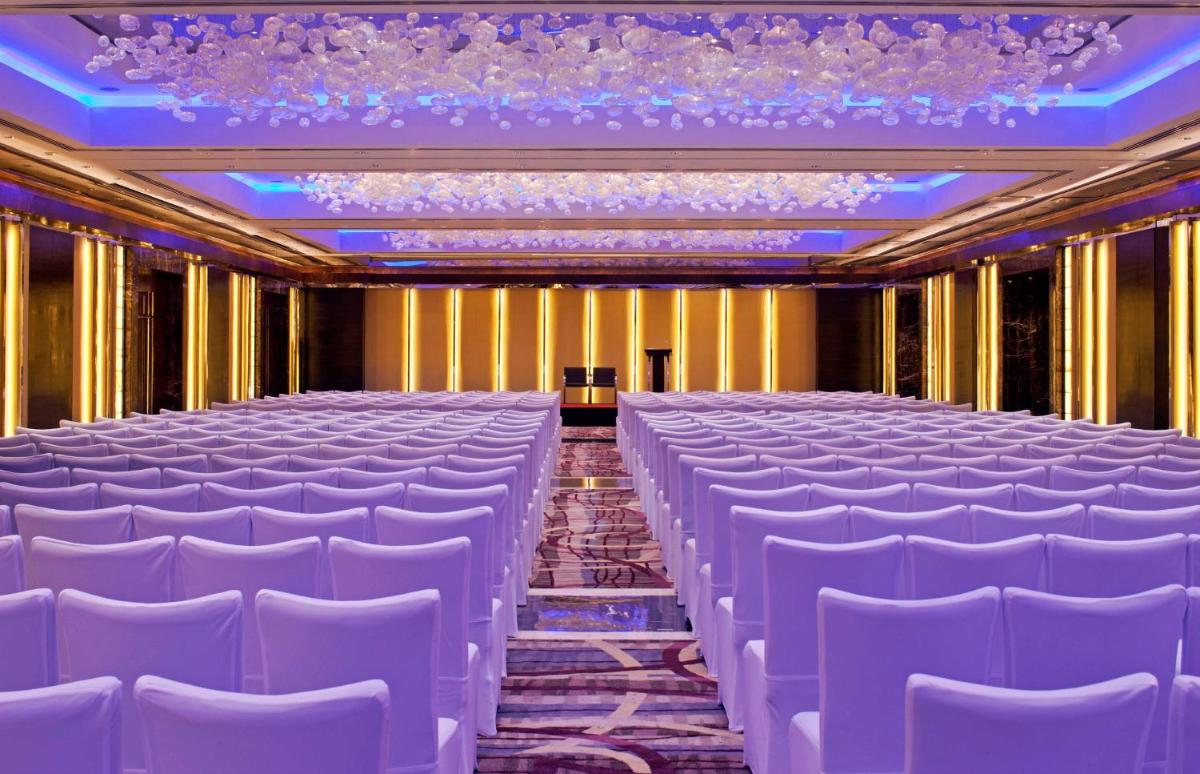 a row of white chairs in a room with a stage at Radisson Blu Plaza Delhi Airport in New Delhi a row of white chairs in a room with a stage at Radisson Blu Plaza Delhi Airport in New Delhi