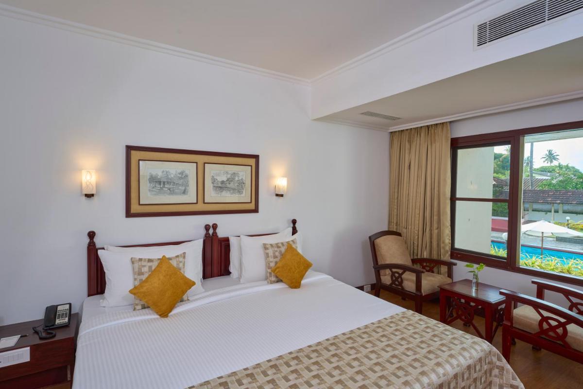 a bedroom with a bed and a desk and a window at Casino Hotel - CGH Earth, Cochin in Cochin