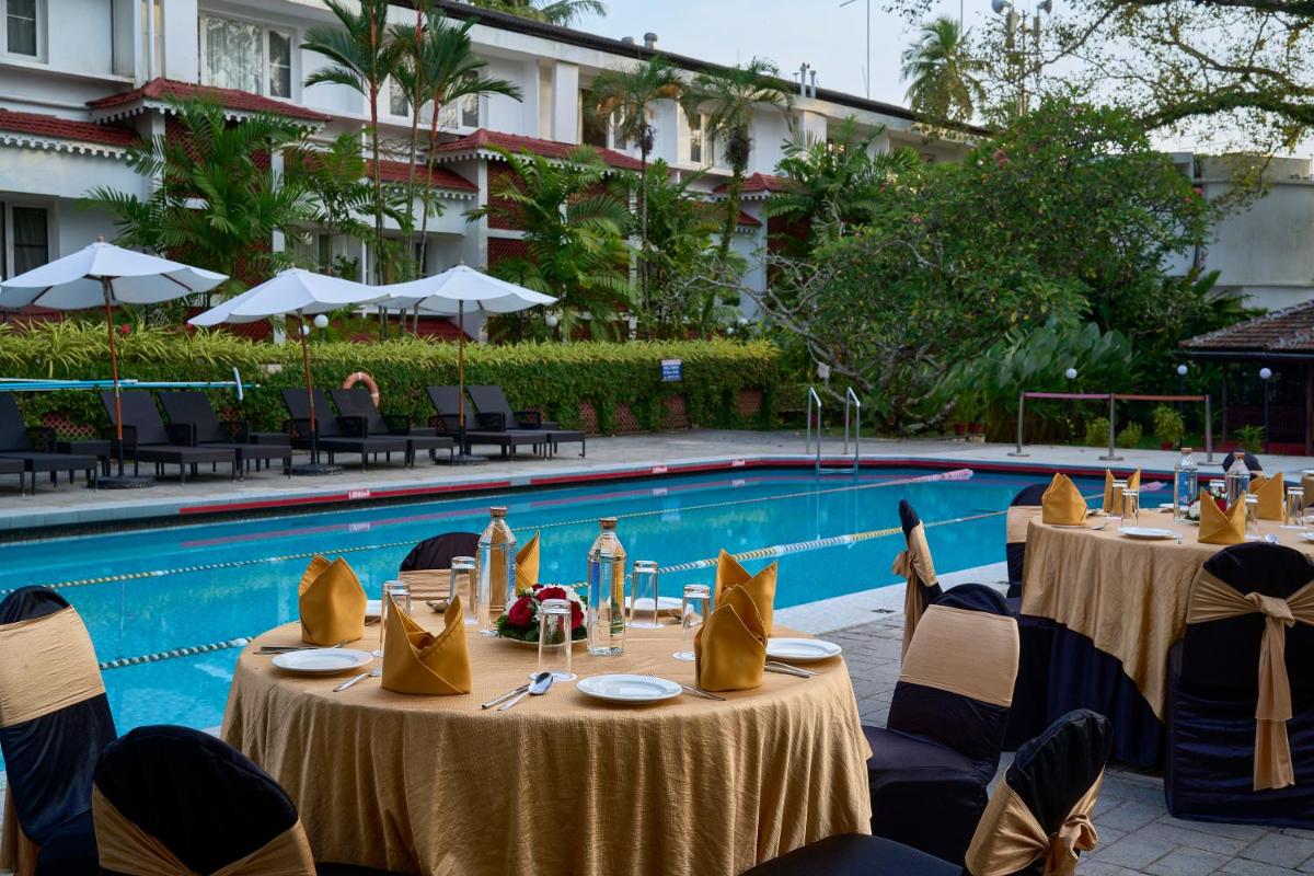 a poolside restaurant with tables and chairs next to a pool at Casino Hotel - CGH Earth, Cochin in Cochin