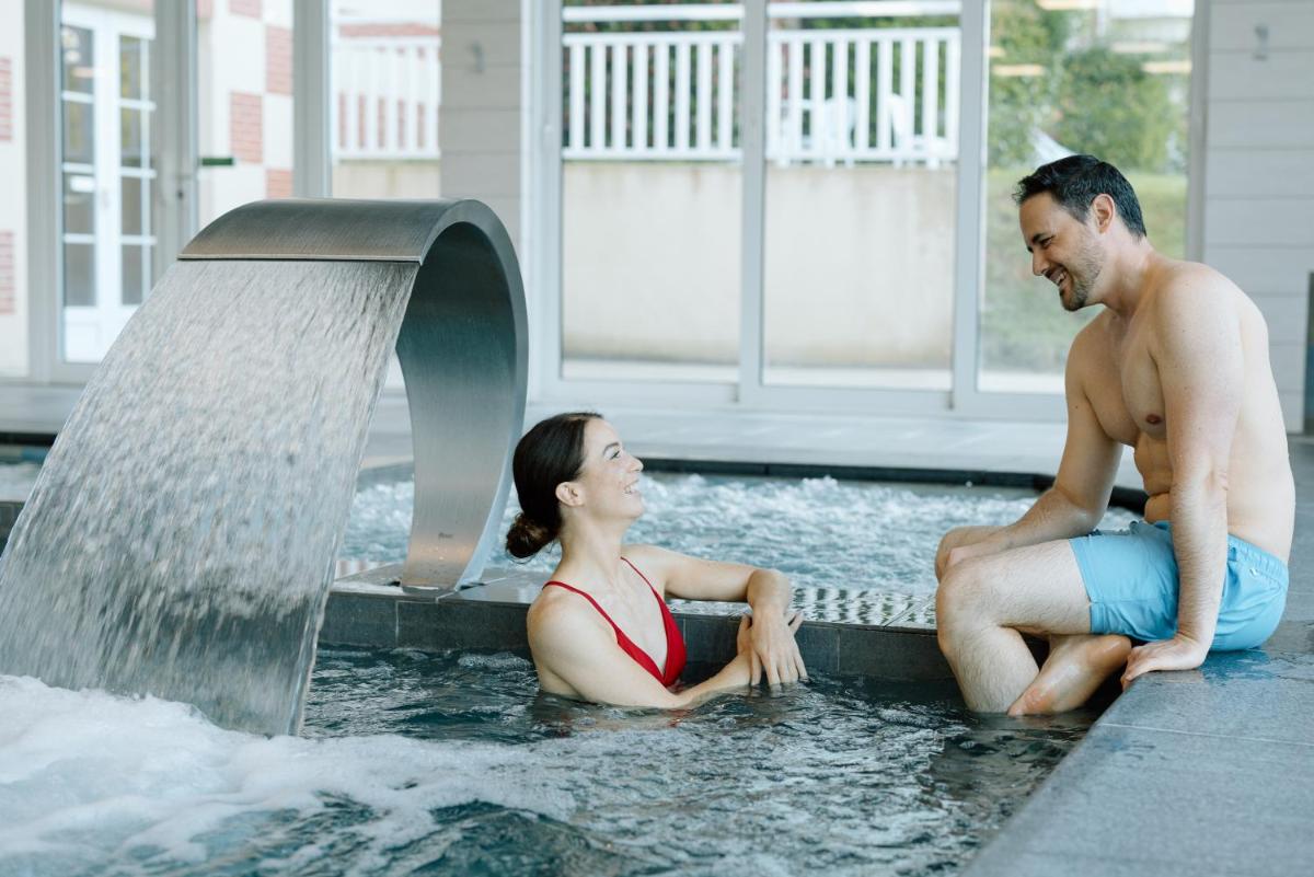 un homme et une femme assis dans une piscine dans l'établissement Résidence b'o cottage - b'o resort thermal & spa, à Bagnoles-de-l'Orne