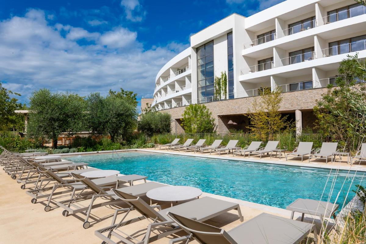 une piscine avec chaises longues et un bâtiment dans l'établissement Hôtel Horizon Resort Massane & Spa, à Baillargues