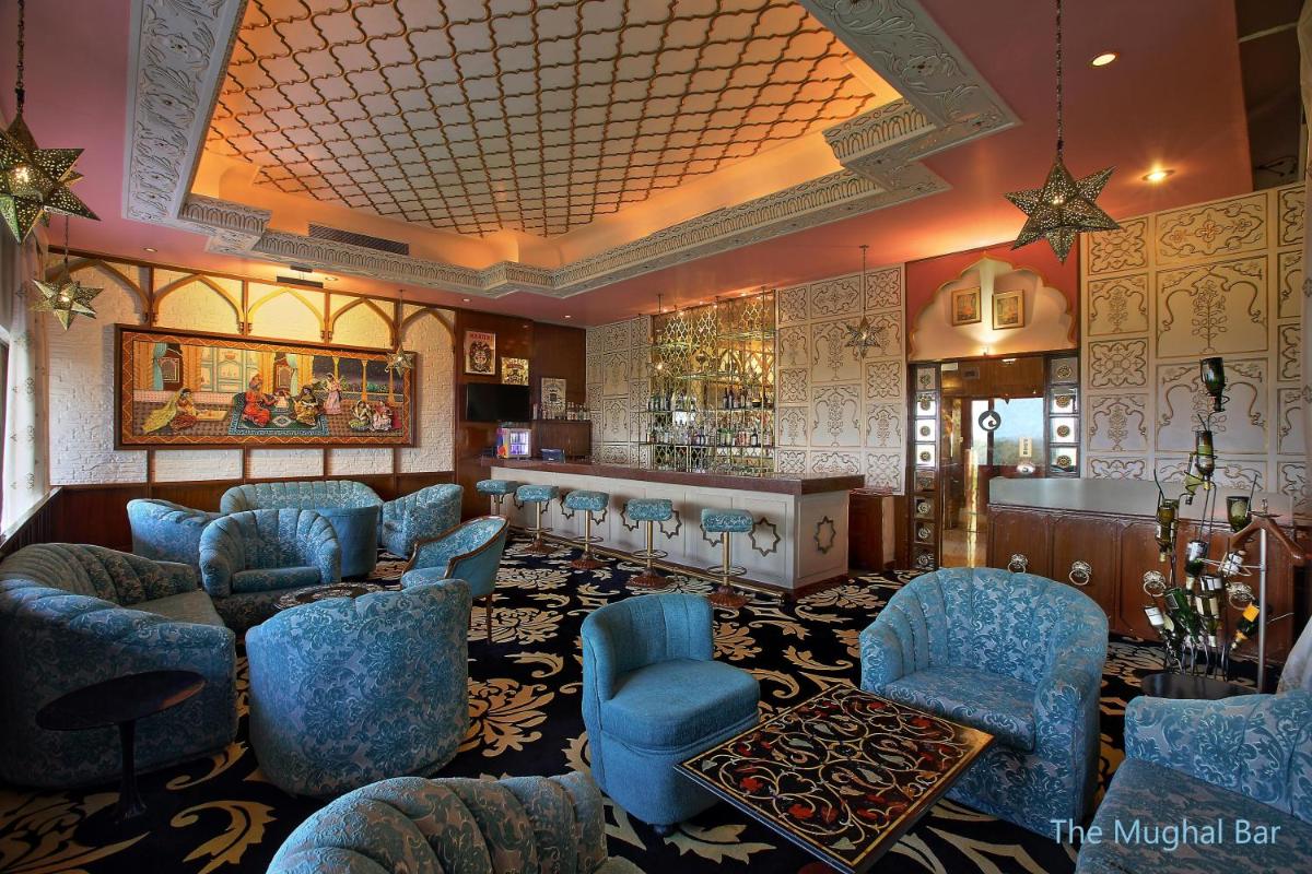 a waiting room with blue chairs and a bar at Hotel Clarks Shiraz in Agra