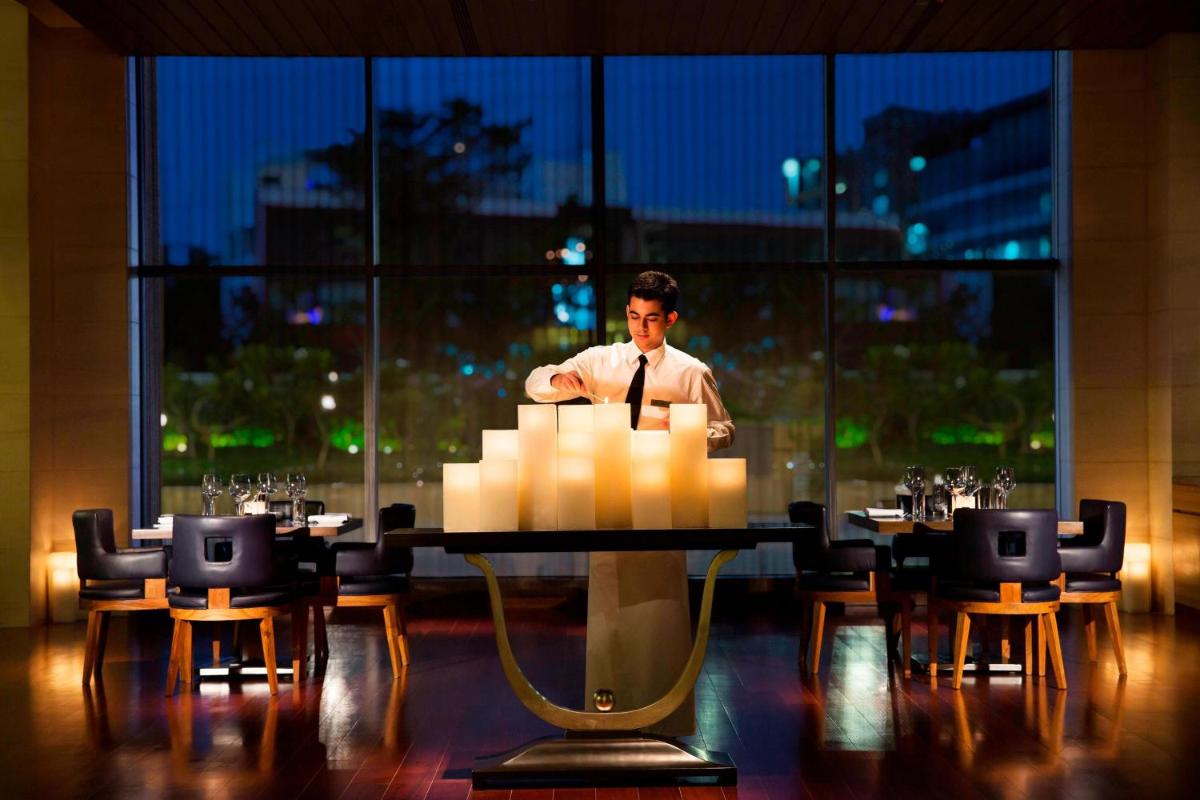 a man in a tie standing at a table in a room at Bengaluru Marriott Hotel Whitefield in Bengaluru