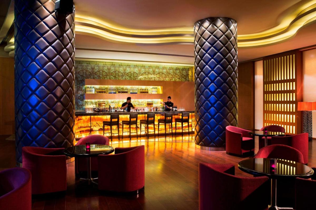 a bar in a hotel with red chairs and tables at Bengaluru Marriott Hotel Whitefield in Bengaluru
