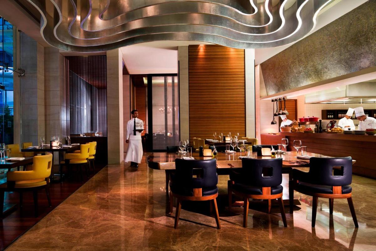 a restaurant with tables and chairs and a chef in the background at Bengaluru Marriott Hotel Whitefield in Bengaluru