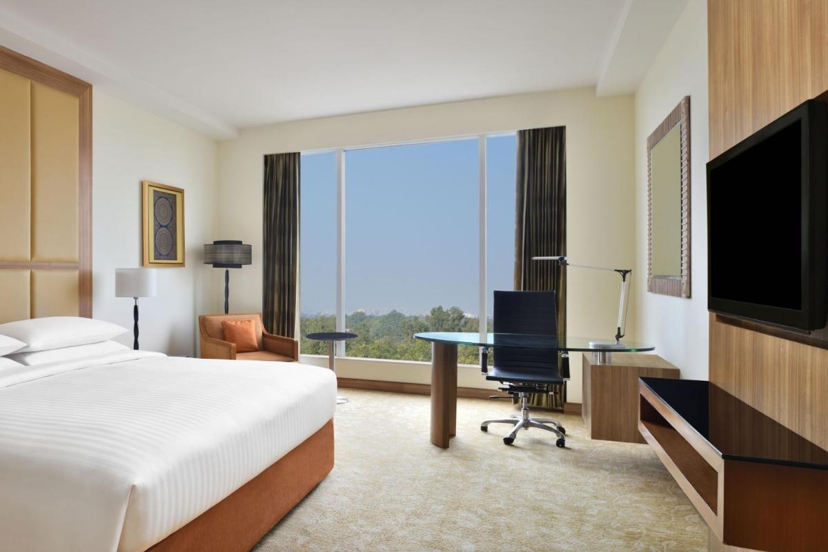 a hotel room with a bed and a desk and a television at Bengaluru Marriott Hotel Whitefield in Bengaluru