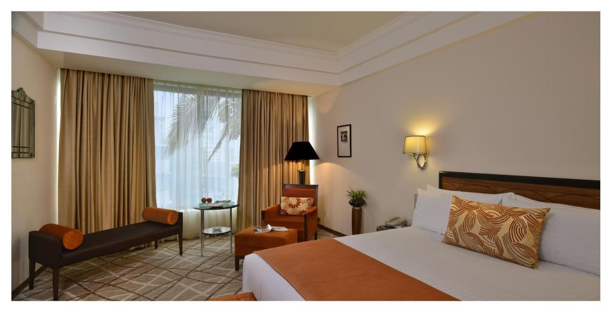 a hotel room with a bed and a chair and a window at Hotel Marine Plaza in Mumbai