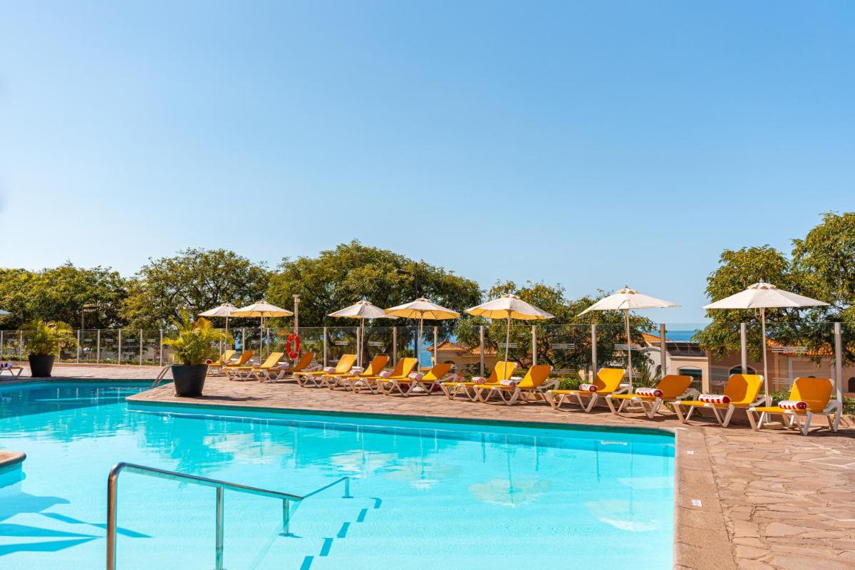 uma piscina com cadeiras e guarda-sóis em Muthu Raga Madeira Hotel no Funchal