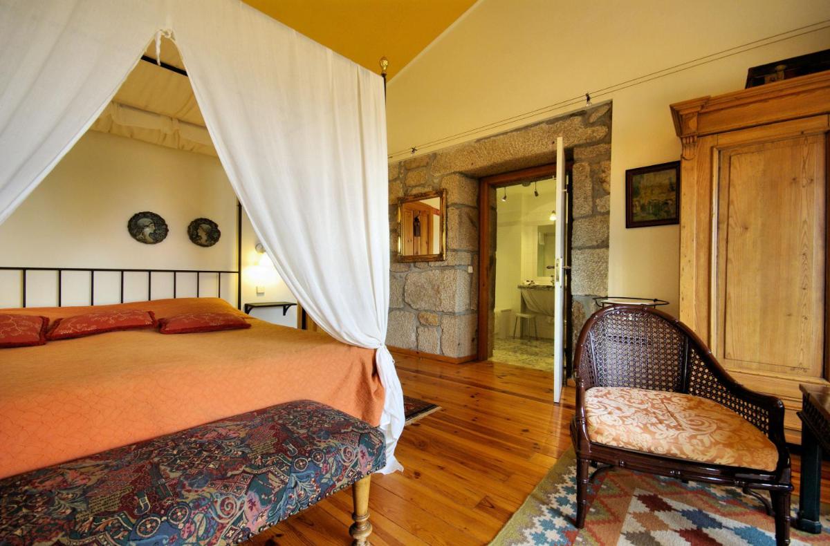 um quarto com uma cama de dossel e uma cadeira em Hotel Rural Quinta da Geia em Aldeia das Dez