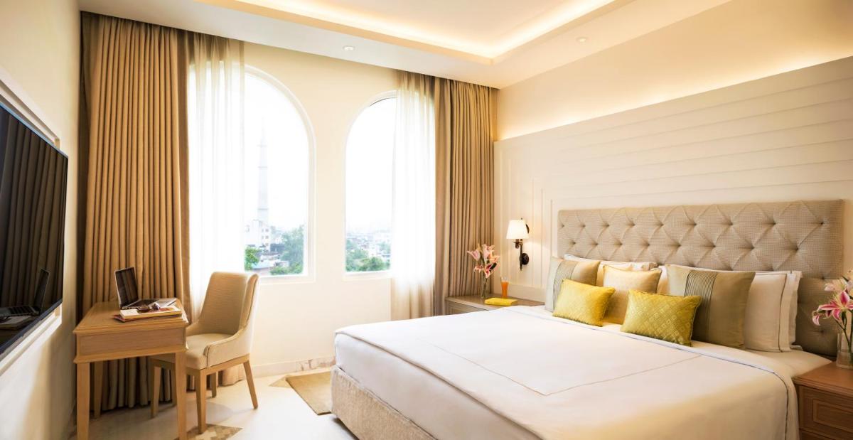 a bedroom with a bed and a desk and a window at Taj Ganges Varanasi in Varanasi