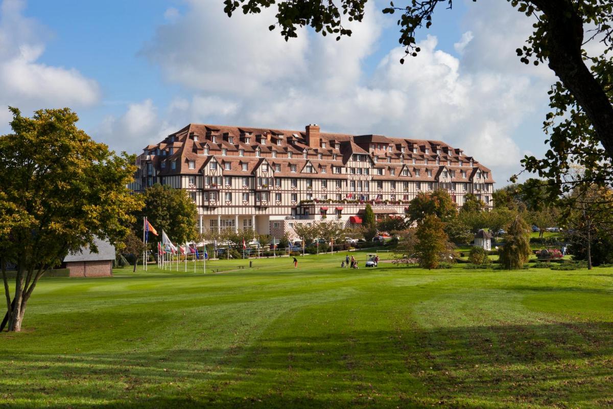 un grand bâtiment dans un parc avec un champ verdoyant dans l'établissement Hôtel Barrière L'Hôtel du Golf, à Deauville