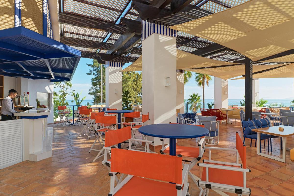 Un restaurante con sillas y mesas de color naranja y un escritorio. en H10 Estepona Palace, en Estepona