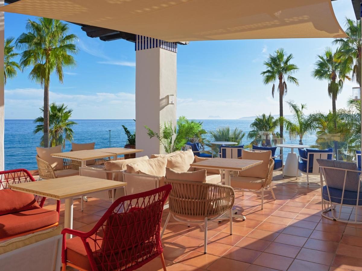 Un patio con mesas y sillas y el mar. en H10 Estepona Palace, en Estepona