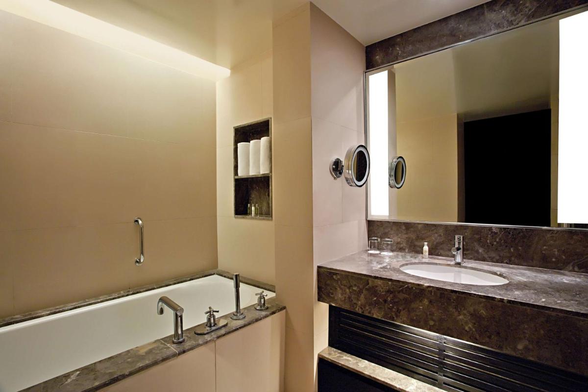 a bathroom with a tub and a sink and a mirror at DoubleTree Suites by Hilton Bengaluru Outer Ring Road in Bengaluru