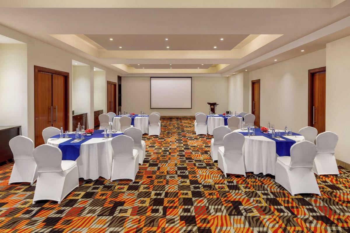 a conference room with tables and white chairs and a screen at DoubleTree by Hilton Gurgaon New Delhi NCR in Gurgaon