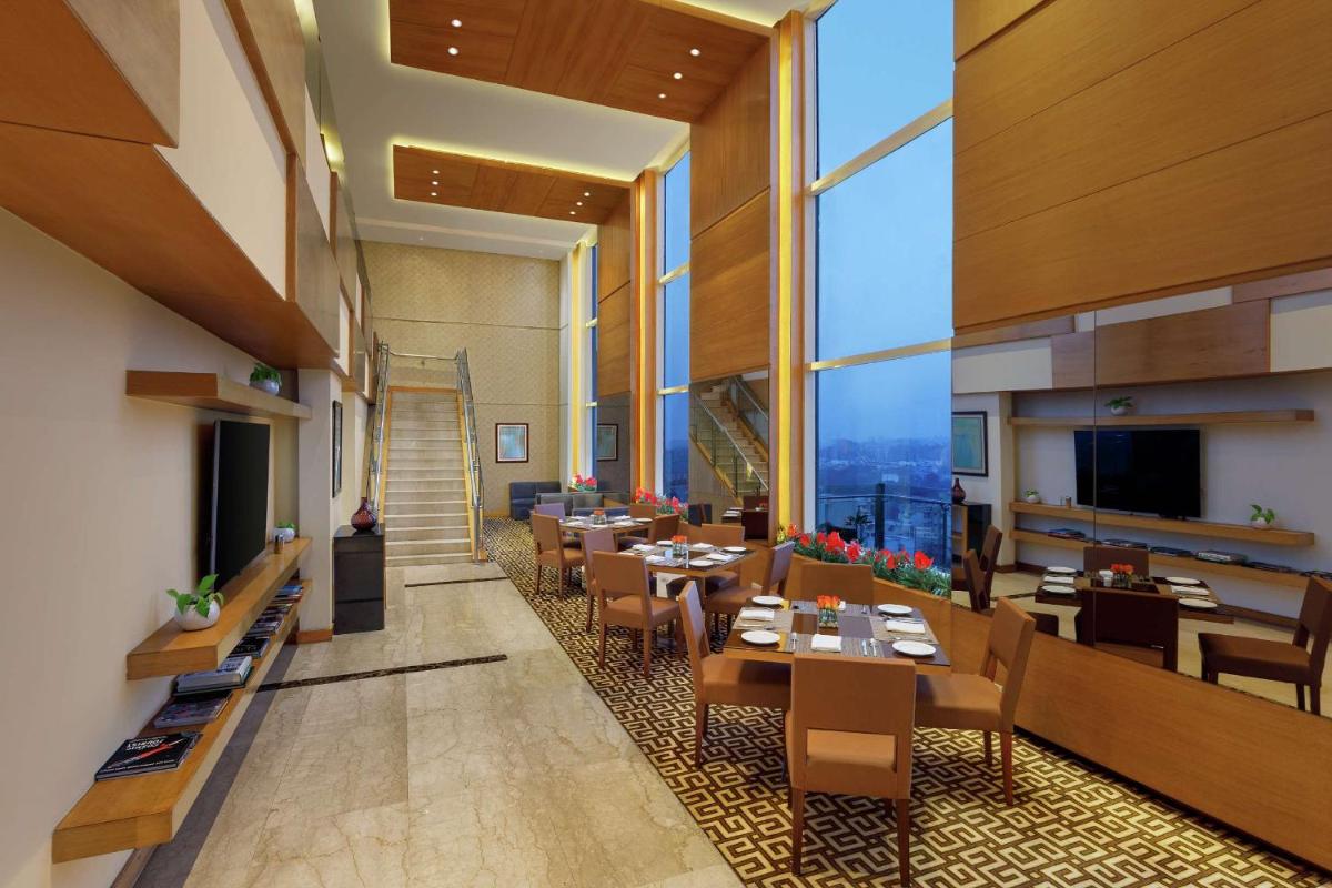 a restaurant with tables and chairs and large windows at DoubleTree by Hilton Gurgaon New Delhi NCR in Gurgaon