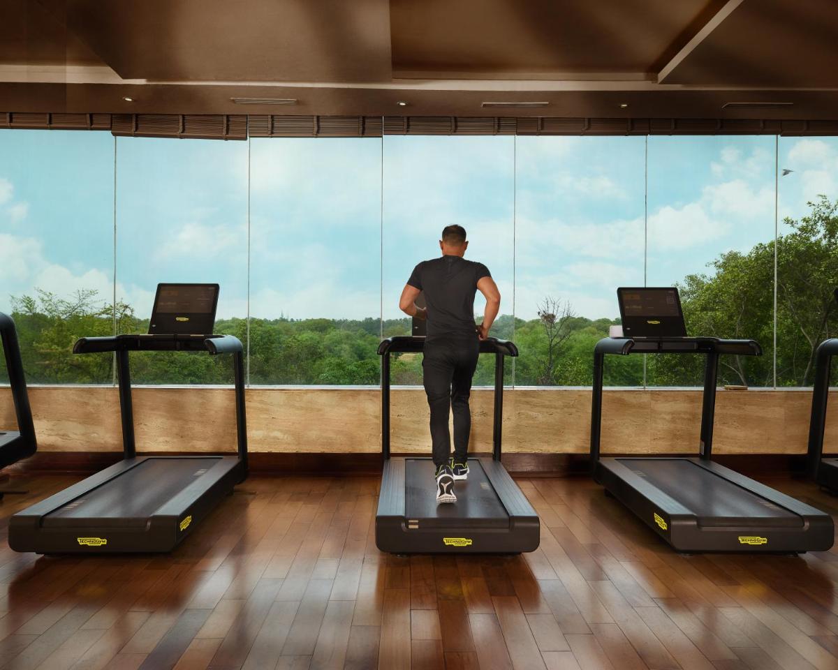 a man standing on a treadmill in front of a window at The Leela Ambience Gurugram Hotel & Residences - The Luxury Urban Sanctuary in Gurgaon