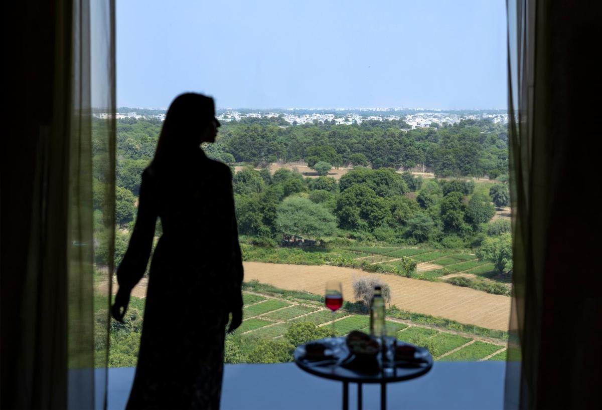 a woman standing in a window looking out at a view at The Leela Ambience Gurugram Hotel & Residences - The Luxury Urban Sanctuary in Gurgaon