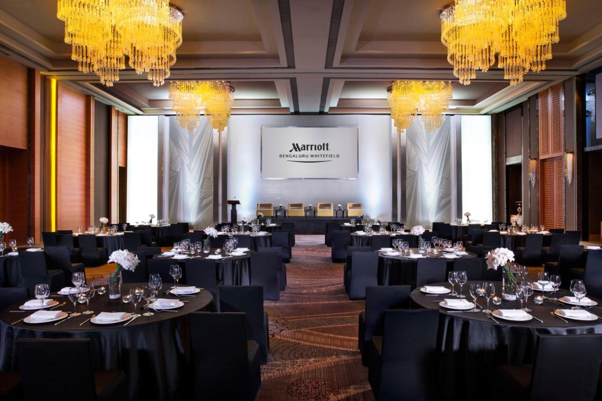 a ballroom with black tables and chairs and chandeliers at Bengaluru Marriott Hotel Whitefield in Bengaluru