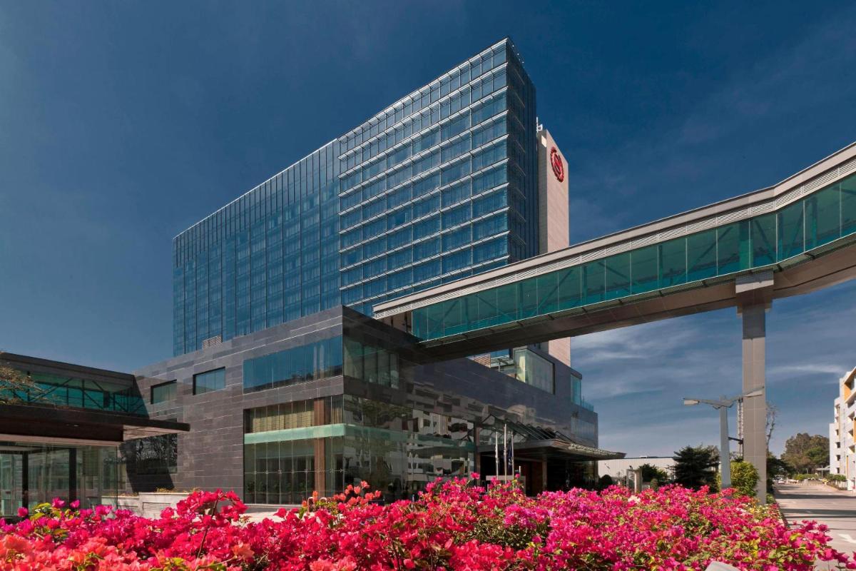 a tall building with pink flowers in front of it at Sheraton Grand Bangalore Hotel at Brigade Gateway in Bengaluru