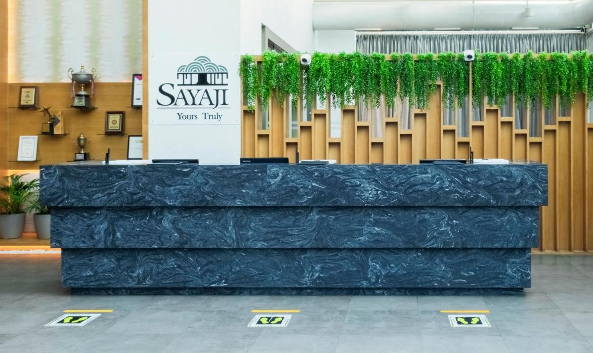 a lobby with a large blue counter with green plants at Sayaji Pune in Pune