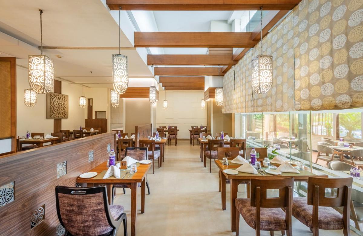 a restaurant with wooden tables and chairs and a large window at Sayaji Pune in Pune