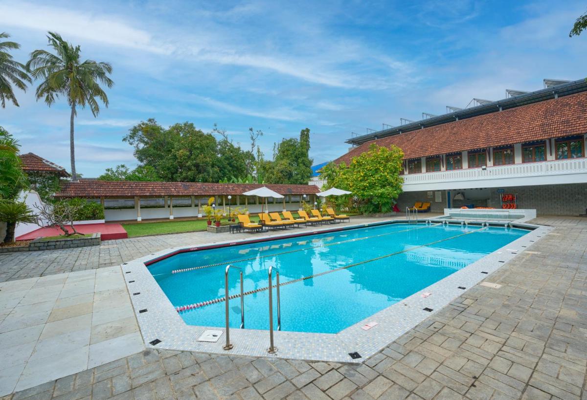 a large swimming pool with chairs and a building at Casino Hotel - CGH Earth, Cochin in Cochin