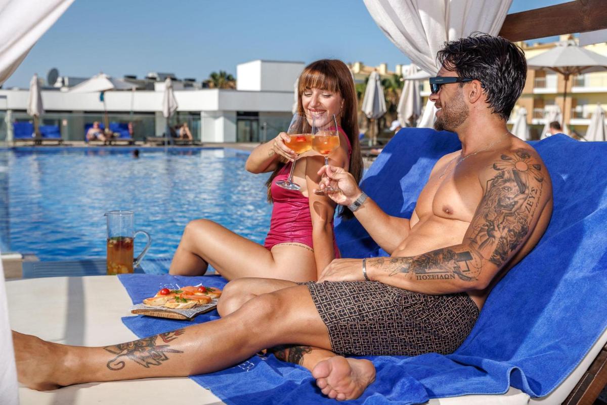 Um homem e uma rapariga sentados numa espreguiçadeira a comer pizza. em Jupiter Marina Hotel - Couples & Spa em Portimão