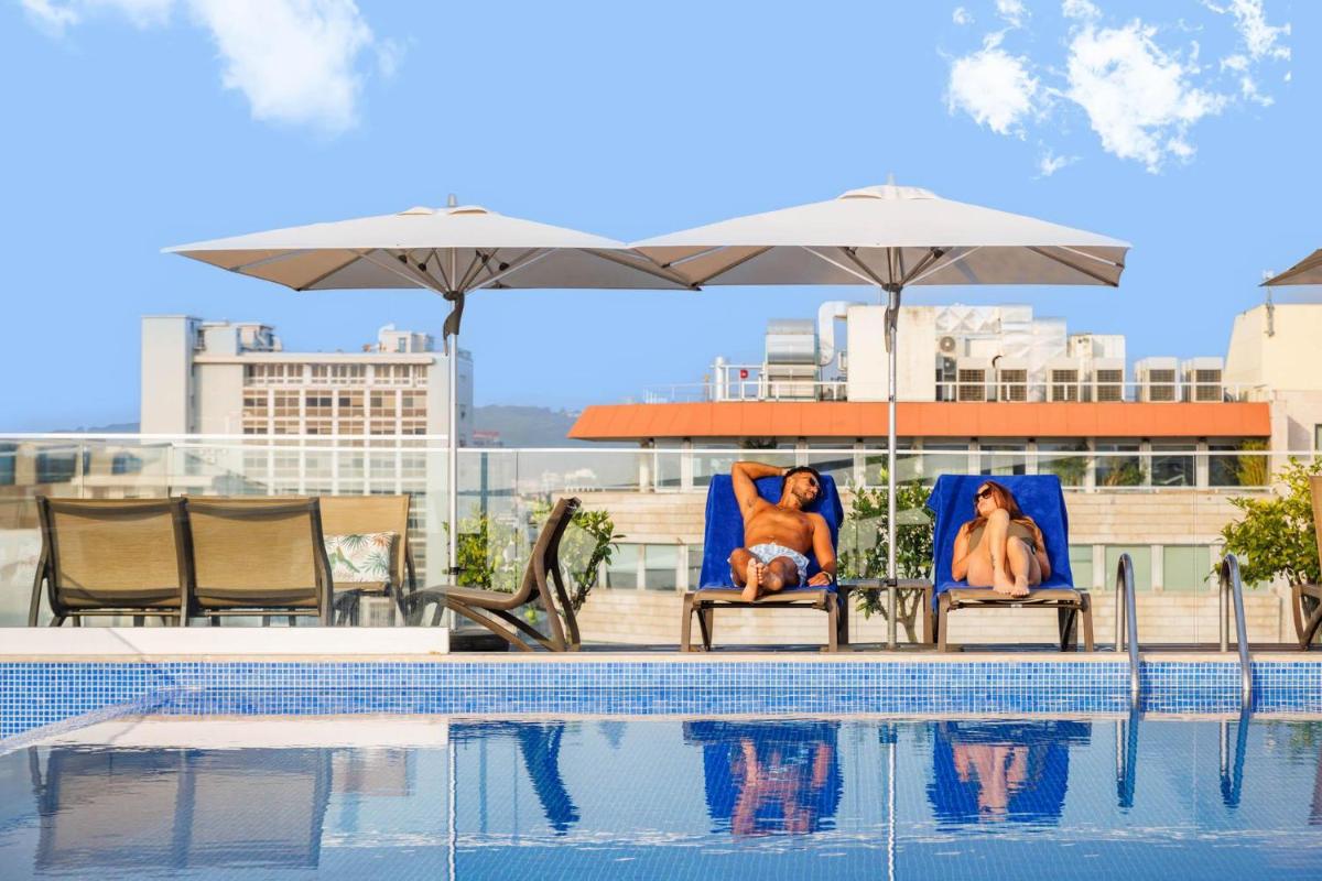 duas mulheres sentadas em cadeiras ao lado de uma piscina em Jupiter Lisboa Hotel - Rooftop & Spa em Lisboa