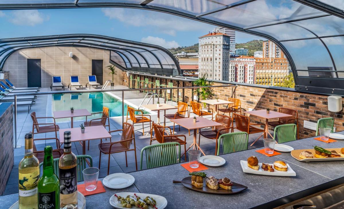 Un balcón con mesas y sillas y una piscina. en Axel Hotel Bilbao - Adults Only, en Bilbao
