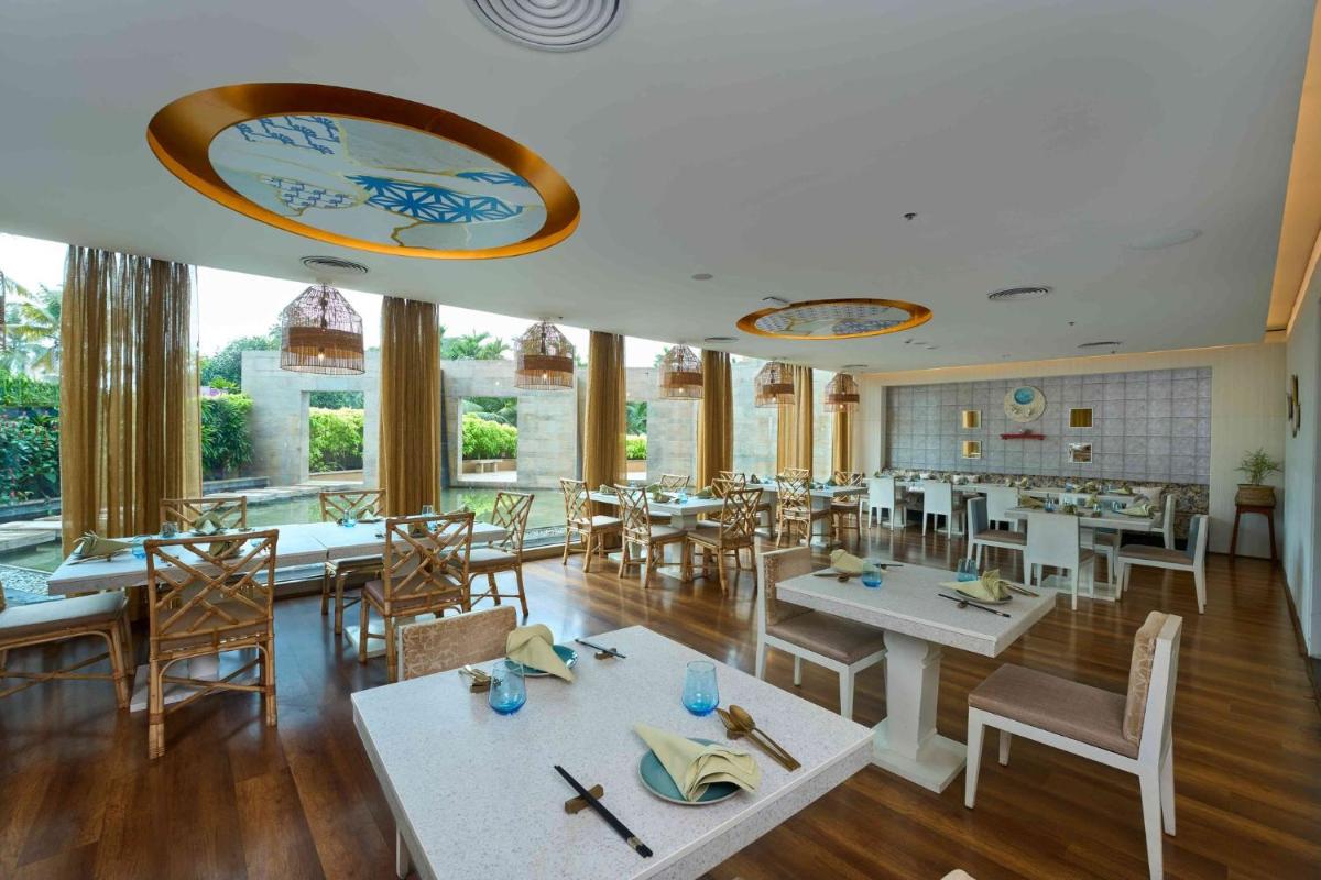 a restaurant with white tables and chairs and windows at Crowne Plaza Kochi by IHG in Cochin