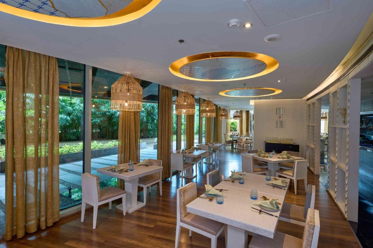 a restaurant with white tables and chairs and windows at Crowne Plaza Kochi by IHG in Cochin