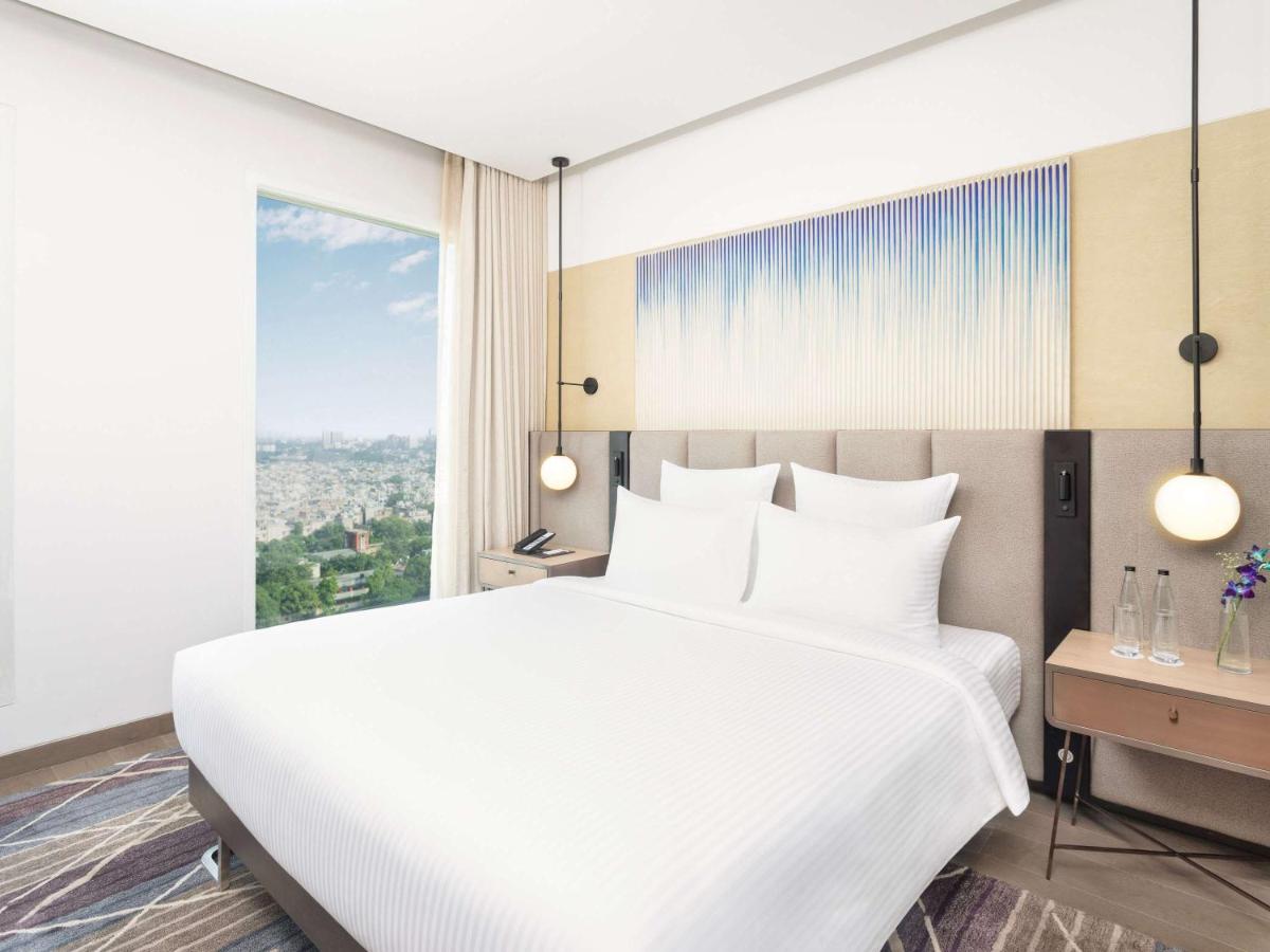 a bedroom with a white bed and a large window at Novotel New Delhi City Centre in New Delhi a bedroom with a white bed and a large window at Novotel New Delhi City Centre in New Delhi