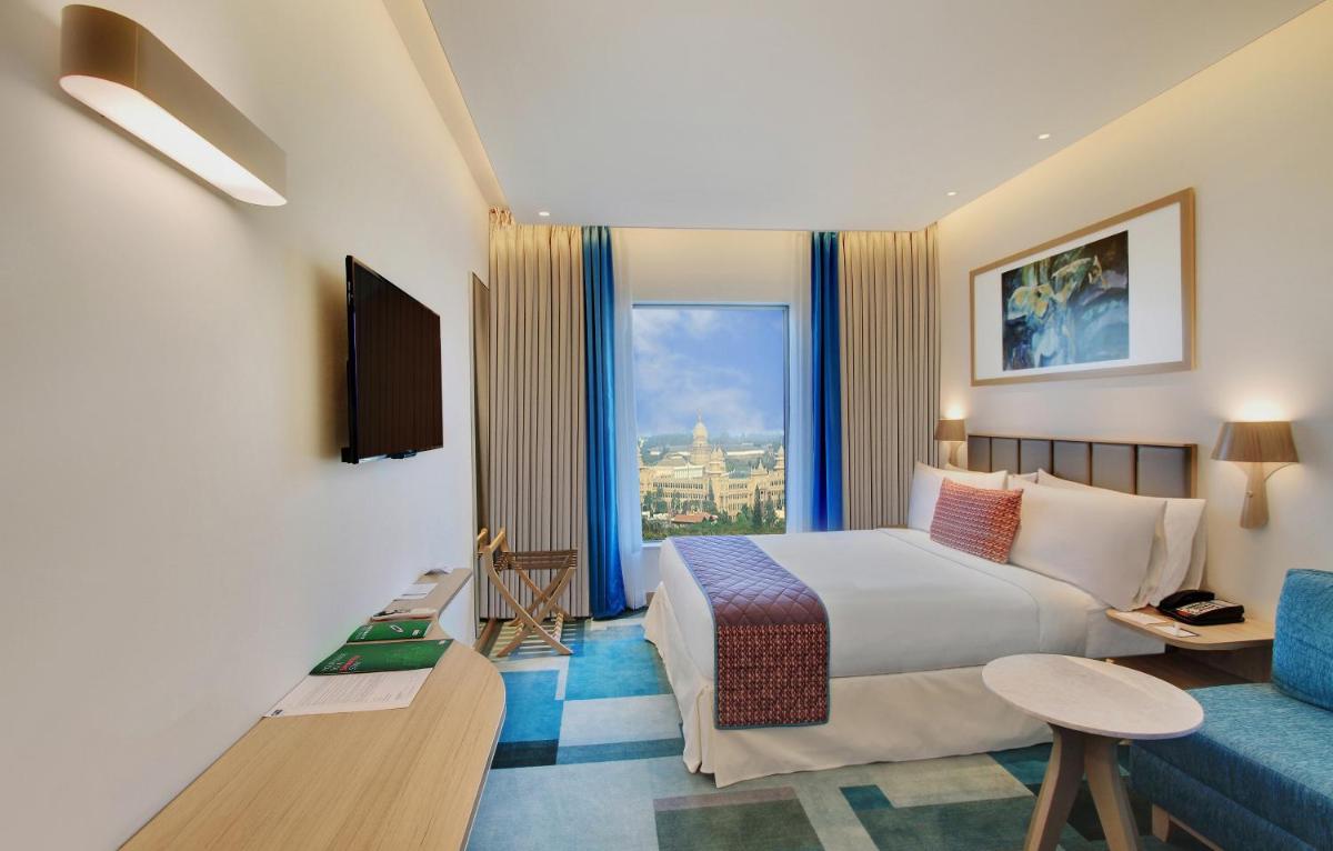 a hotel room with a large bed and a blue couch at Holiday Inn Bengaluru Racecourse by IHG in Bengaluru a hotel room with a large bed and a blue couch at Holiday Inn Bengaluru Racecourse by IHG in Bengaluru