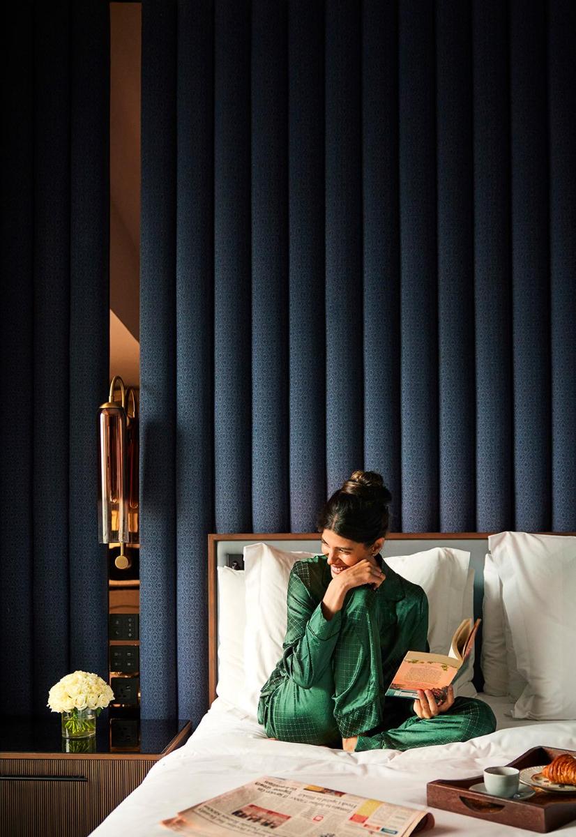 a woman sitting on a bed reading a book at Four Seasons Hotel Mumbai in Mumbai