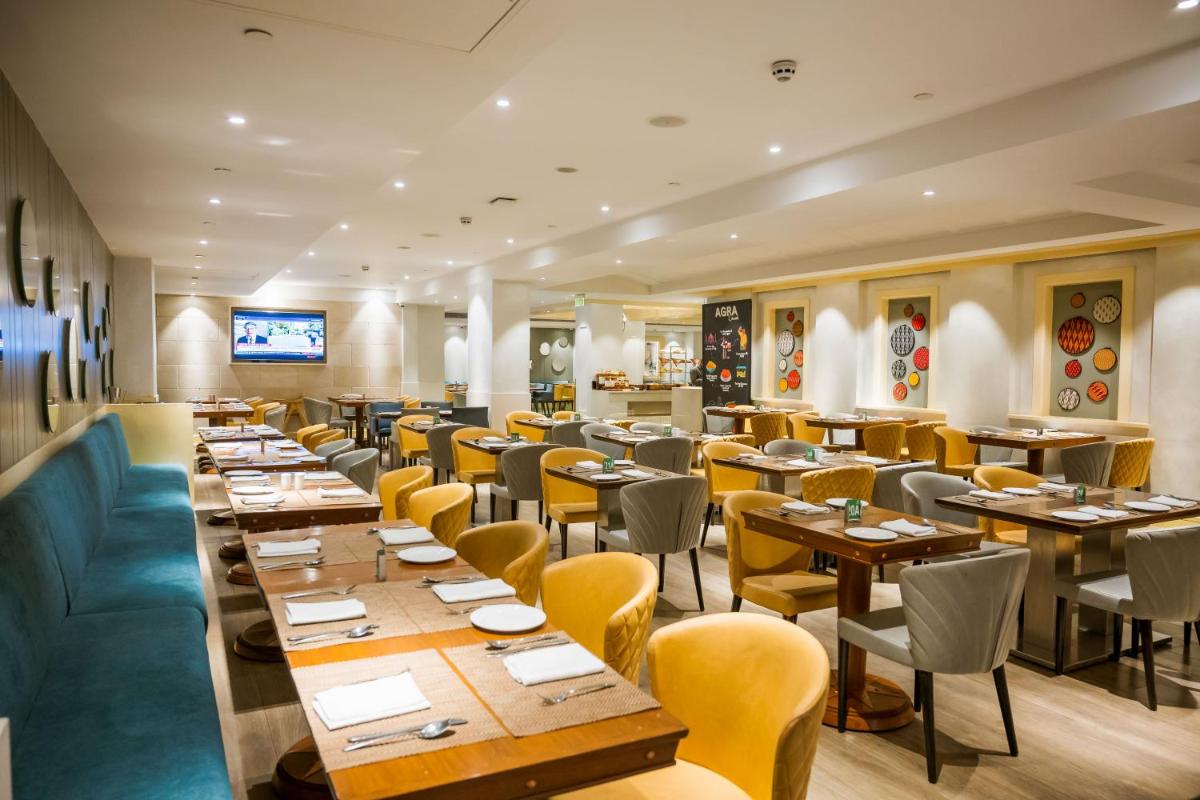 a restaurant with wooden tables and yellow chairs at Holiday Inn Agra MG Road an IHG Hotel in Agra