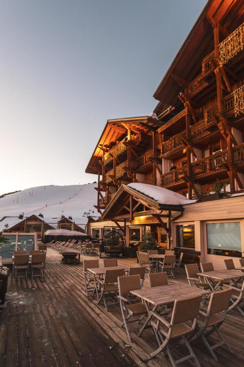 une terrasse en bois avec des chaises et des tables ainsi qu'un bâtiment dans l'établissement Hôtel Au Chamois d'Or by Les Etincelles, à L'Alpe-d'Huez