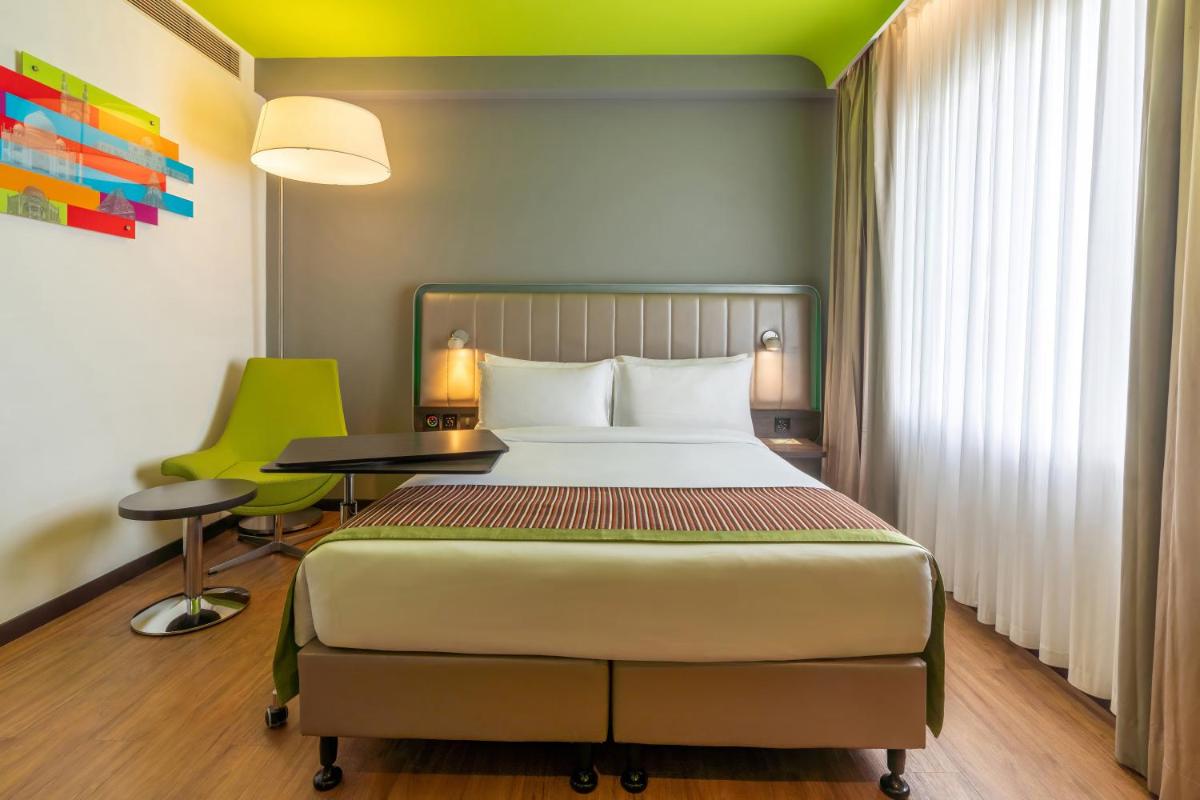 a bedroom with a bed and a table and a green chair at Park Inn by Radisson,South Delhi in New Delhi a bedroom with a bed and a table and a green chair at Park Inn by Radisson,South Delhi in New Delhi