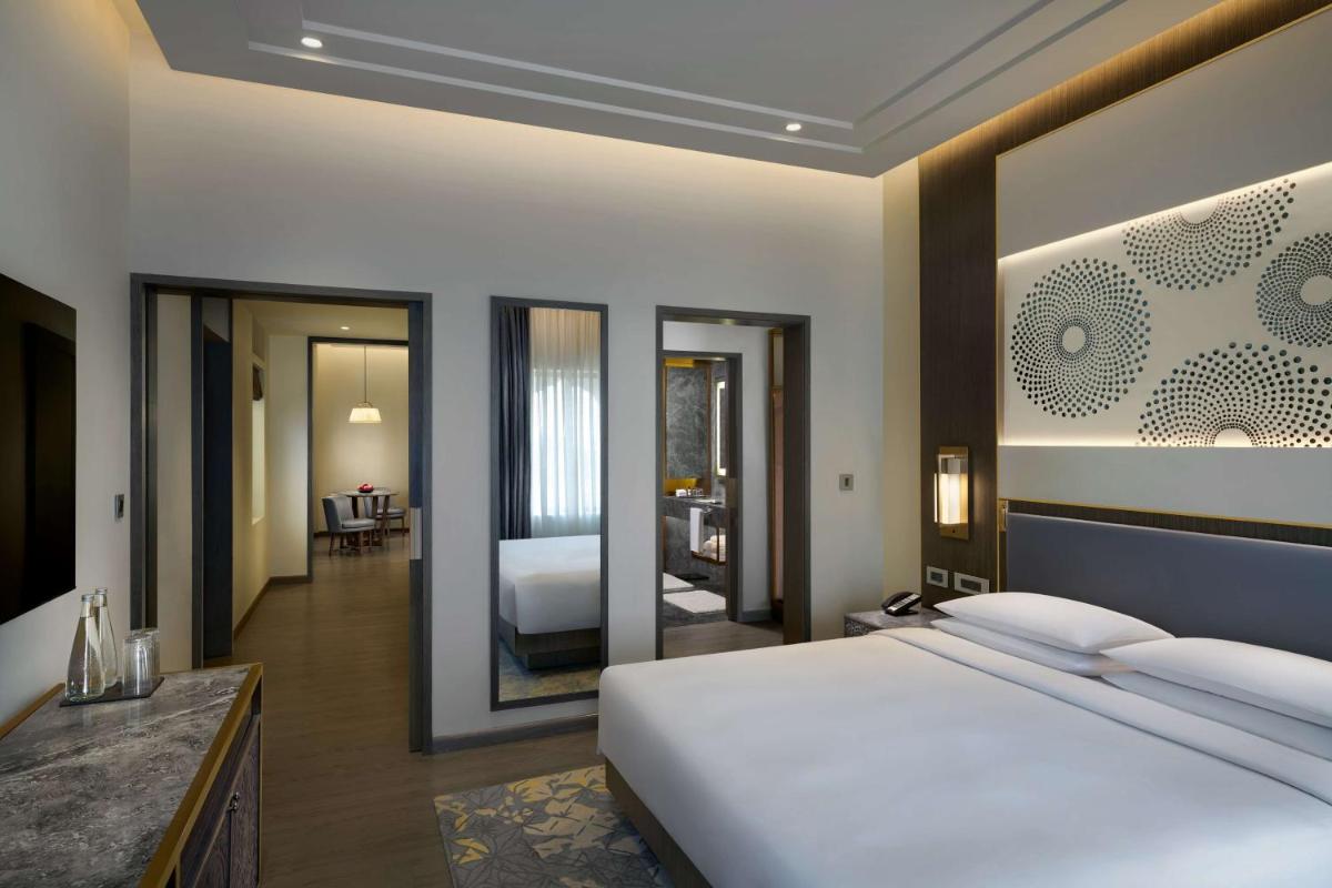 a bedroom with a large white bed and a bathroom at Hyatt Regency Jaipur Mansarovar in Jaipur a bedroom with a large white bed and a bathroom at Hyatt Regency Jaipur Mansarovar in Jaipur