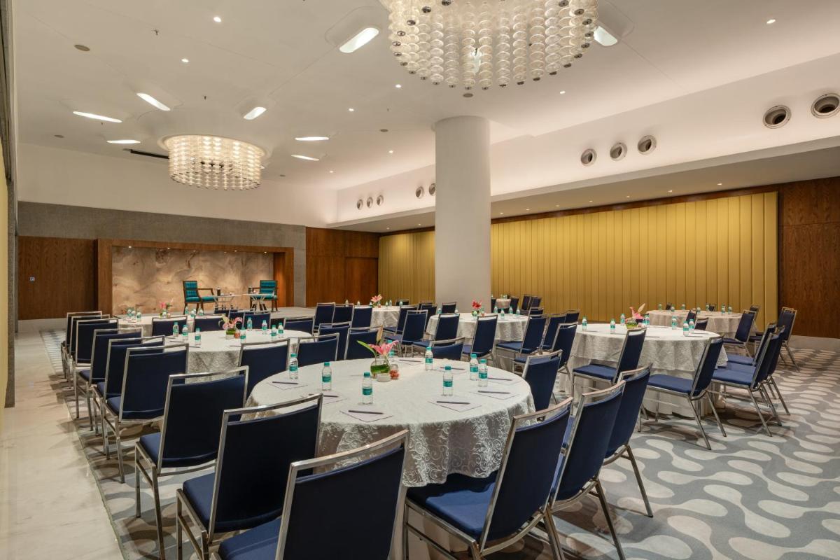 a conference room with long tables and chairs and chandeliers at Avasa Hotel in Hyderabad