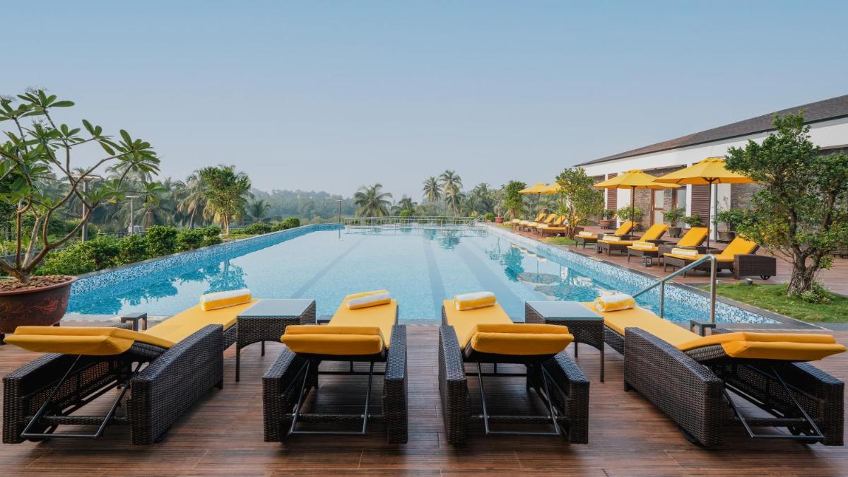 a swimming pool with tables and chairs next to a building at Gateway Goa, Palolem in Palolem